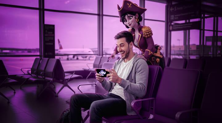 HOMBRE DE ALREDEDOR DE 20 AÑOS SENTADO EN UNA SALA DE ESPERA DE UN AEROPUERTO MIENTRAS QUE ESTÁ ESPERANDO; ESTÉ EN SU TELÉFONO JUGANDO EN PLAYUZU Y DETRÁS DE ÉL ESTÉ UN PERSONAJE DEL SLOT LOCK & LOOT GIGABLOX