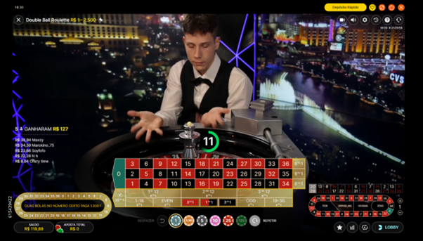 Dealer da Double Ball Roulette ao vivo no est&uacute;dio da Evolution, com a roleta em primeiro plano, o painel de apostas vis&iacute;vel e o cen&aacute;rio noturno de Las Vegas iluminado ao fundo. Na tela, cron&ocirc;metro mostrando tempo restante para fazer apostas.